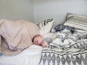 Carson sleeping in a bed next to a pink pillow and covered by a black and while blanket