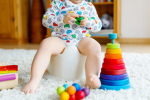 Child in onesie sitting on a potty surrounded by toys