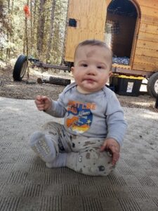 Baby Carson sitting in front of doghouse trailer