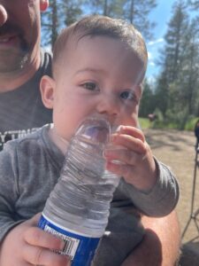 Caleb being held by his dad and chewing on a waterbottle.