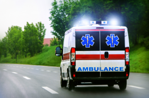 Photo of an ambulance with lights on driving away on a multilane road.