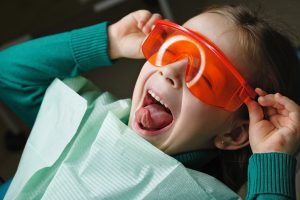 Little girl sits in dental chair and wears protective glasses. 