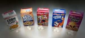 Photo of mini boxes of cereal with sugar cubes in front of them.