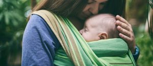 Mom in a the outdoors carrying her newborn in a green wrap carrier