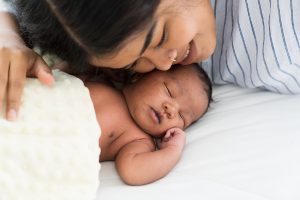 Top view mother kissing her newborn baby on bed. Young mom or nurse taking care newborn in the hospital