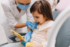 Side view portrait of little girl looking at mirror in pediatric dentistry after dental surgery.