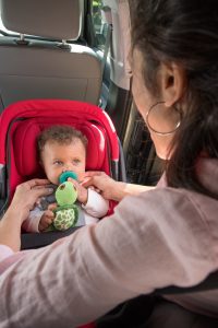 Mother in pink sweater adjusting harness of baby in rear-facing car seat