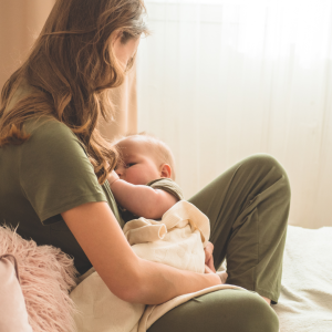 Woman with long hair and green shirt breastfeeding her baby