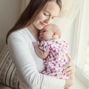 Happy mom in white blouse holding baby in strawberry patterned outfit