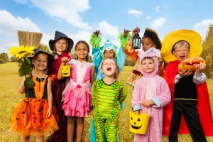 Happy excited kids in Halloween costumes stand close on green grass of the field