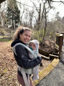 Smiling Natalia holding Isaiah in a carrier looking at the camera