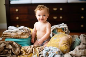 Baby smiling at the camera sitting surrounded by stacks of cloth diapers