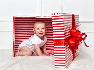 Baby in a white onesie inside a red and white striped box