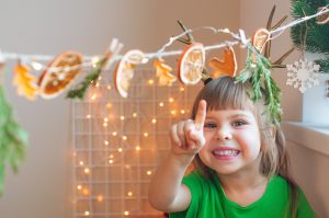 Little girl showing Christmas garland of dried citrus slices in the kids room. Selective focus.