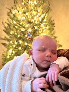 Newborn Isaiah being held in front of a lit Christmas tree