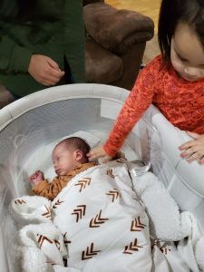 Child patting newborn Isaiah as he sleeps in a bassinet