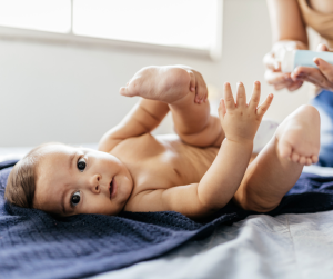 Baby on a blue towel having their diaper changed is looking at the camera