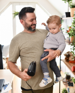 Dad carrying hairdryer in one hand and toddler in the other