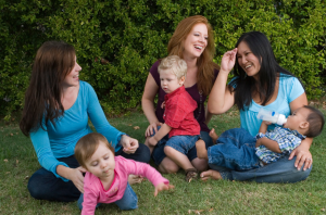 Three moms and toddlers sitting on the ground outside.