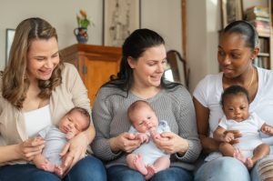 Three moms holding new babies and looking at each other