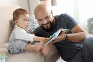 Dad reading book with his little son in living room