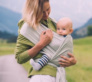 Mother carrying little child in baby sling in green mint color. 