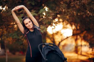 Woman Stretching in the Park Next to a Baby Stroller