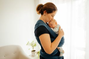 Portrait of lovely and carrying mother with newborn baby in sling. Tired young mother with cute sleeping newborn in baby wrap. Attachment parenting concept.