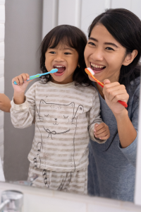 Mom and young child brush teeth together