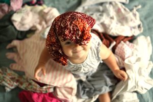 baby playing in big pile of clean clothes looking up at the camera