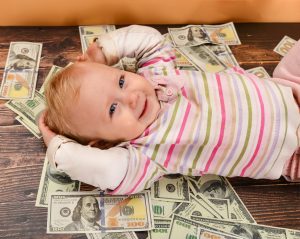 A small child, a girl lies on a wooden background, dollars are falling from above on a child. 