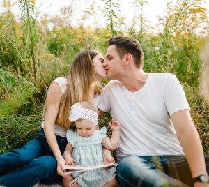 Happy young parents kissing while daughter sits between them with a book