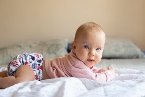 A happy, baby lying on her stomach wearing a cloth diaper