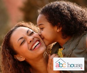 Black child kissing her mother, while mother laughts. ABC House logo in the lower right corner