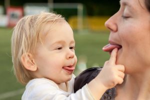 Young child and mother stick out their tongues