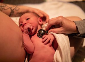 Hands of a midwife are seen checking the health of a newborn baby boy in moments after labor as mother cradles new life