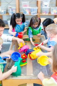 Group of nursery children playing at a water table with their teacher.