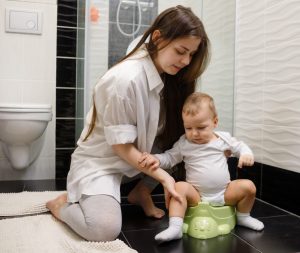 Mom helping her young child sit on a potty