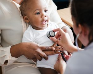 Parent holding baby while doctor listens to their heart.