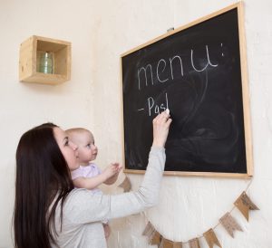 Mom and toddler daughter menu planning on a blackboard with chalk.