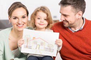 Family portrait of a smiling couple and a child holding a drawing of a house