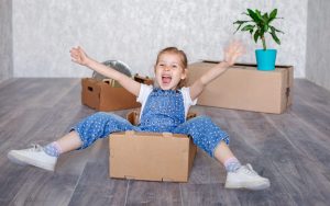 A little blonde girl plays with cardboard boxes. 