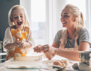 Blond mom teaching her daughter cooking in the kitchen. 