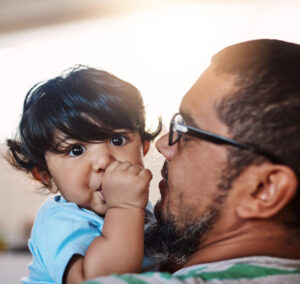 Father holding child. Child sucking thumb and looking at the camera.