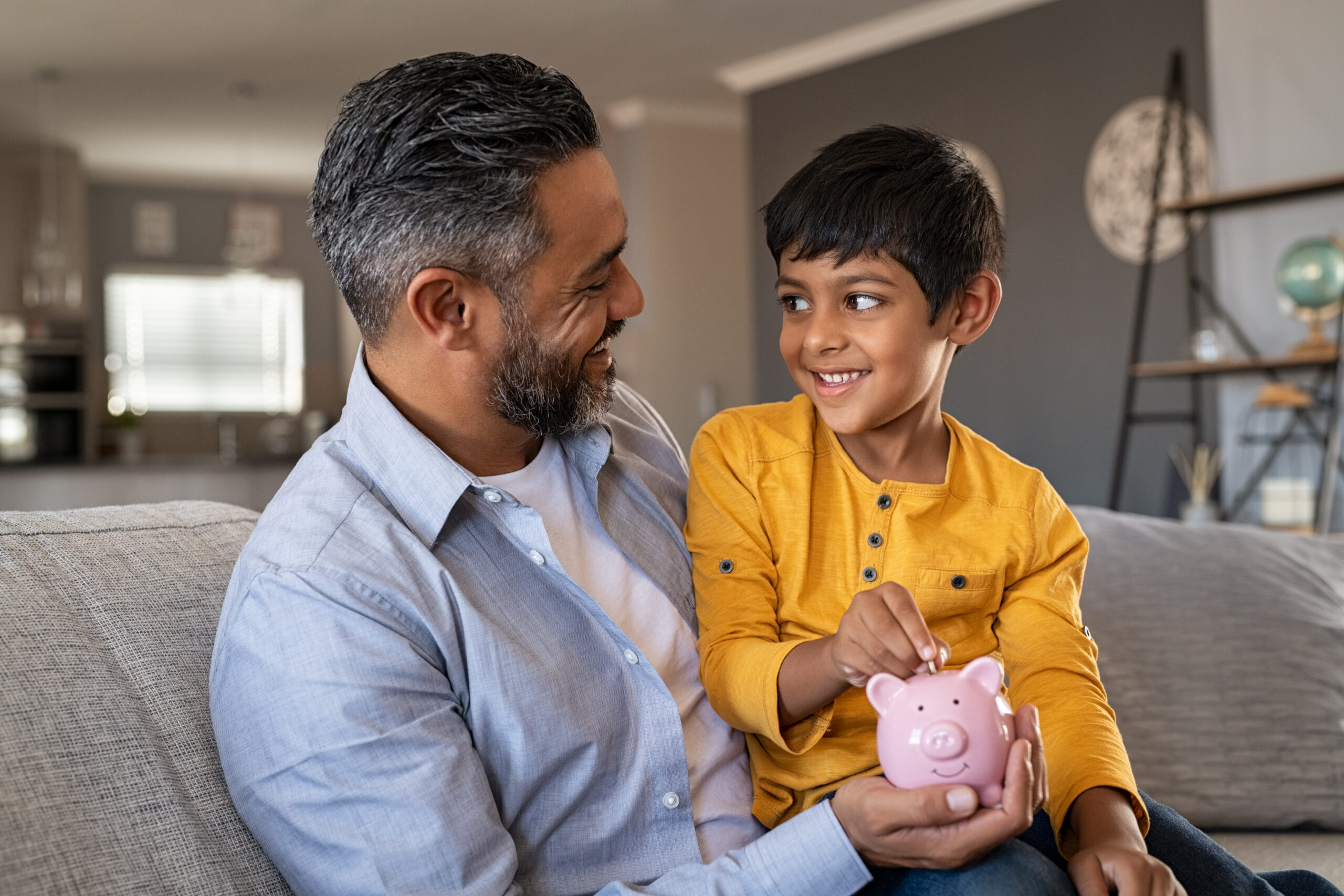 Child sitting on father lap adding coins to a piggybank