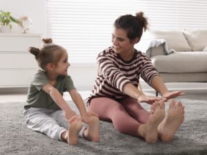 Young mother and her daughter stretching together at home