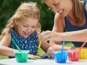 Mother and daughter painting, fun with art and messy with watercolor creativity outdoor.