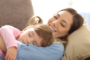 Close up of a proud mother watching her baby sleeping lying on a sofa in the living room at home