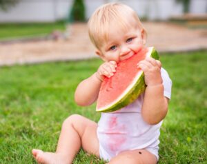 Little one enjoying summer treat with big bite of watermelon.