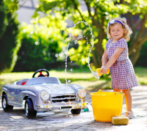 Toddler girl washing car with soap and water, having fun with splashing and playing with sponge